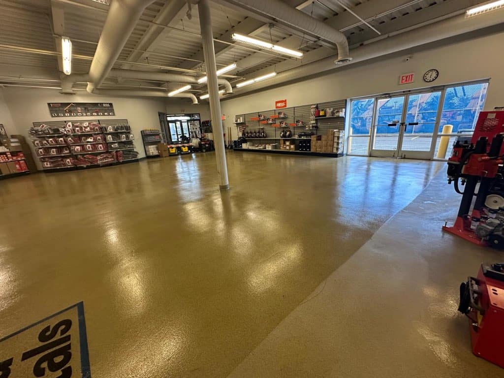 A clean, spacious showroom with polished floors, shelves of automotive or industrial equipment on the left, various tools and supplies displayed, and large glass doors letting in natural light.